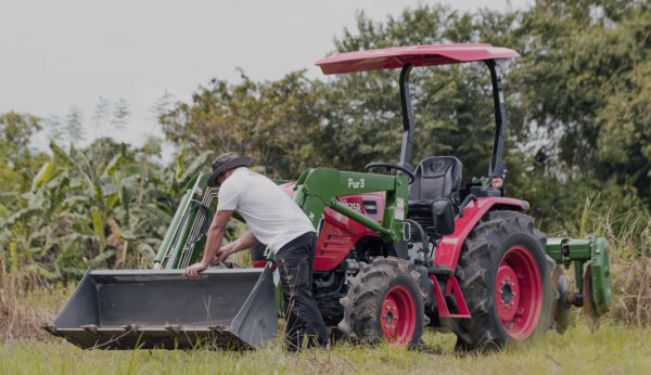 Farmer inspecting the front loader bucket of a red agricultural tractor in a field.